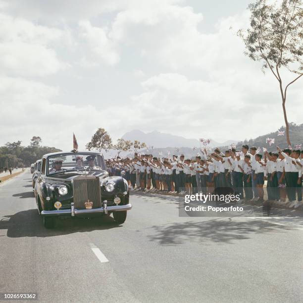 Local schoolchildren wave union flags beside a road as a motorcade, headed by Princess Alexandra's Rolls Royce car, drives past during a royal tour...