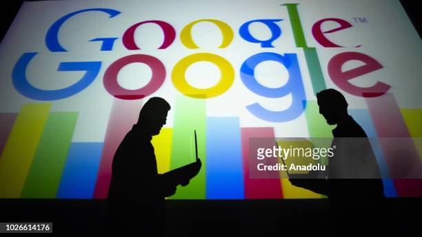 Silhouettes of people holding laptops are seen in front of the logo of 'Google' technology company on the 20th anniversary of Google, in Ankara,...