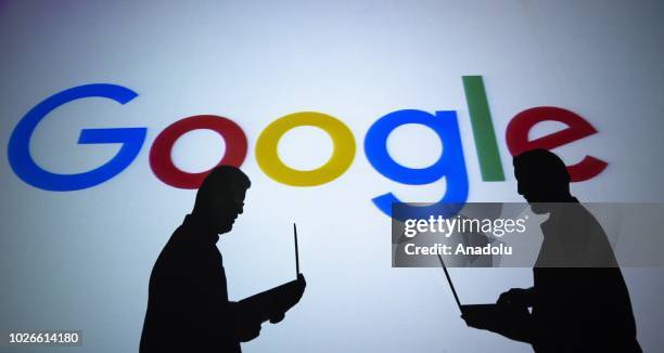 Silhouettes of people holding laptops are seen in front of the logo of 'Google' technology company on the 20th anniversary of Google, in Ankara,...