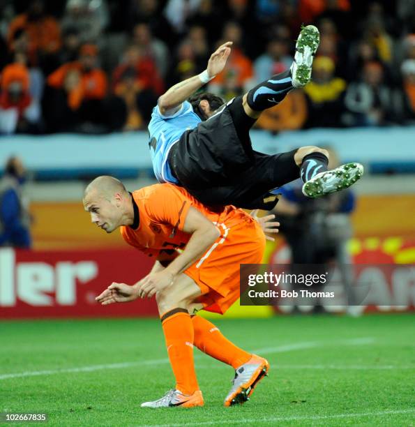 Sebastian Abreu of Uruguay falls over John Heitinga of the Netherlands during the 2010 FIFA World Cup South Africa Semi Final match between Uruguay...