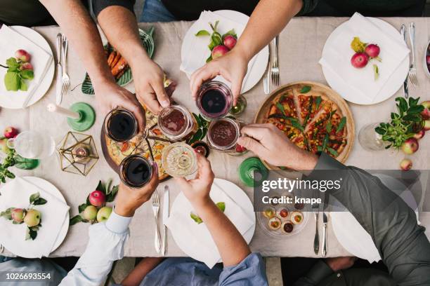 freunde genießen ein abendessen zusammen rösten in wein und bier - friends toasting above table stock-fotos und bilder