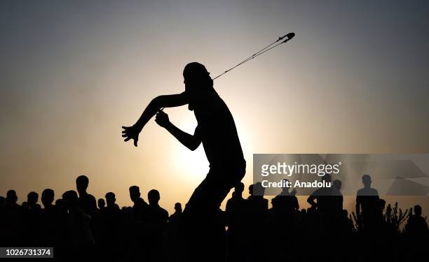 Silhouette of a Palestinian throwing a rock with a slingshot in response to Israeli forces' intervention in a protest against U.S. Move to cut...