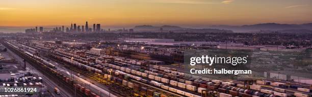 aerial panorama of floodlit freight train yard in vernon with downtown la skyline at sunset - vernon ca stock pictures, royalty-free photos & images