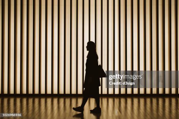 silhouette of woman walking in front of striped illuminated wall - mall interior photos et images de collection