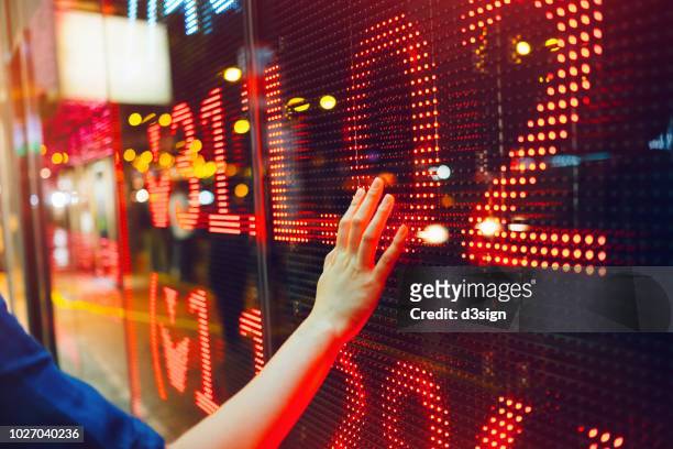woman's hand on stock exchange market display screen board on the street showing stock drops in red colour - red stock photos et images de collection