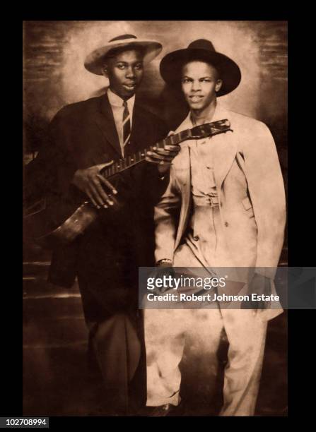 Two men wearing suits and hats, one holding a guitar, pose for a portrait, circa 1930s. The identity of the men is disputed, it has been suggested...