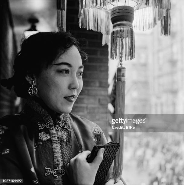Woman in traditional dress watches Chinese New Year celebrations from a balcony in Chinatown, Manhattan, New York City, 28th January 1960.