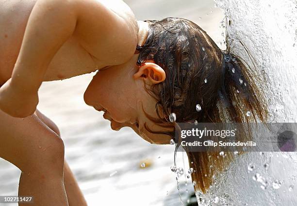 Two-year-old Carmen Brumos of Valencia, Spain, lowers her head into a jet of water near the Washington Monument on the National Mall July 8, 2010 in...