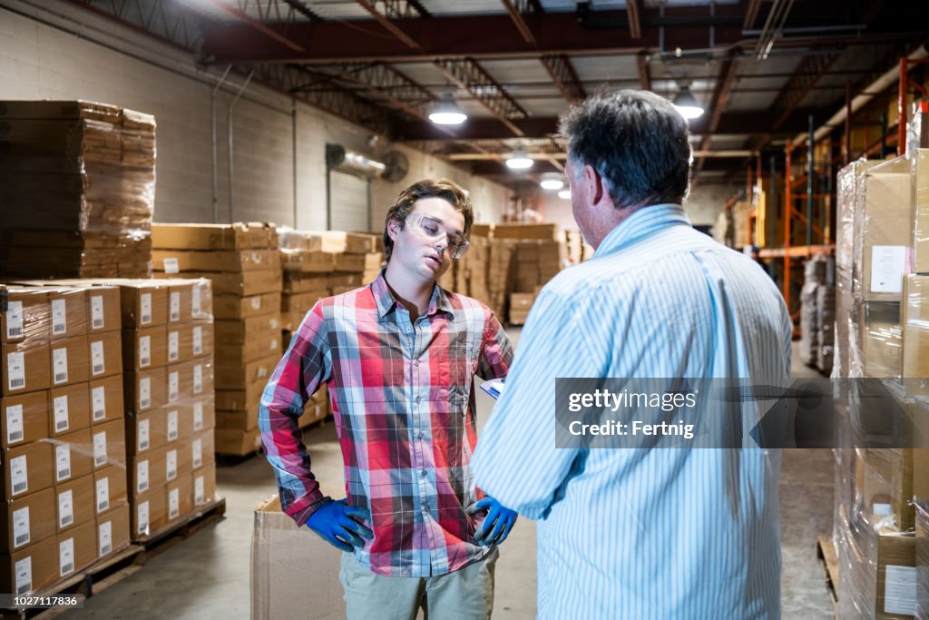 Un jefe de almacén, conversa con un joven trabajador de almacén.