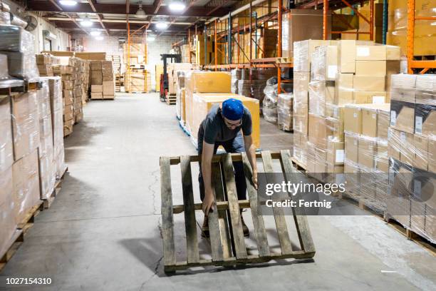 een mannelijke magazijnmedewerker probeert op te heffen van een pallet in een onveilige manier dat zijn rug kon verwonden - ergonomie stockfoto's en -beelden