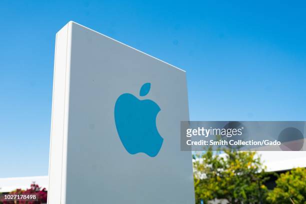 Close-up of blue logo on sign with facade of headquarters buildings in background near the headquarters of Apple Computers in the Silicon Valley,...