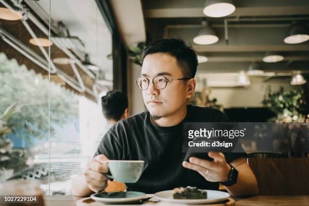 smart young asian man using smartphone and having coffee in cafe - smart windows photos et images de collection