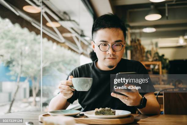 smart young man having a relaxed time enjoying coffee and cake with smartphone in cafe - coffee cake stockfoto's en -beelden