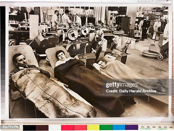 Workers asleep on the factory floor, 1969. A photograph of three workers from the company Cimex, Orpington, Kent, asleep in camp beds set up on the...