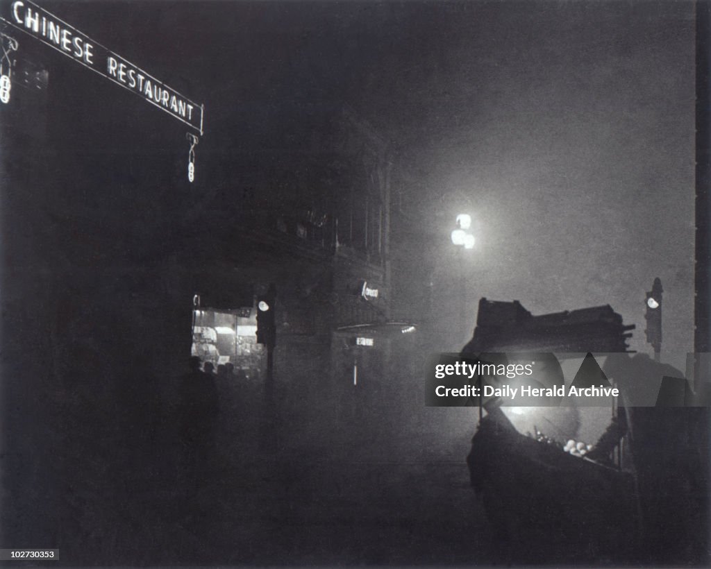 'A foggy Piccadilly partially lit by the light from a fruit seller's stall, 1952.