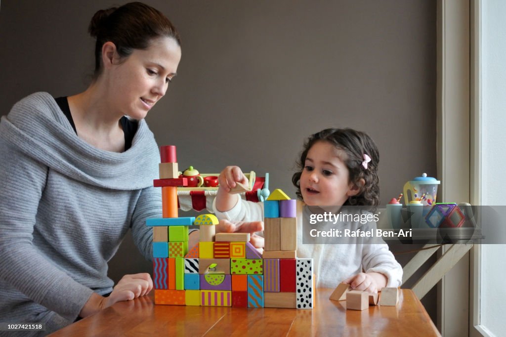 Young Girl is Playing Building Bricks with her Mother