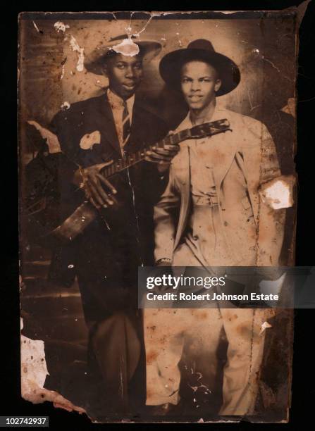 Two men wearing suits and hats, one holding a guitar, pose for a portrait, circa 1930s. The identity of the men is disputed, it has been suggested...
