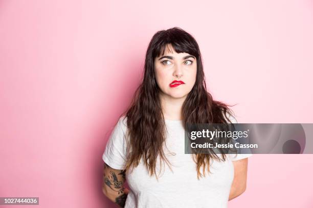 portrait of a woman with tattoos and red lipstick against a pink background - confusion stock pictures, royalty-free photos & images