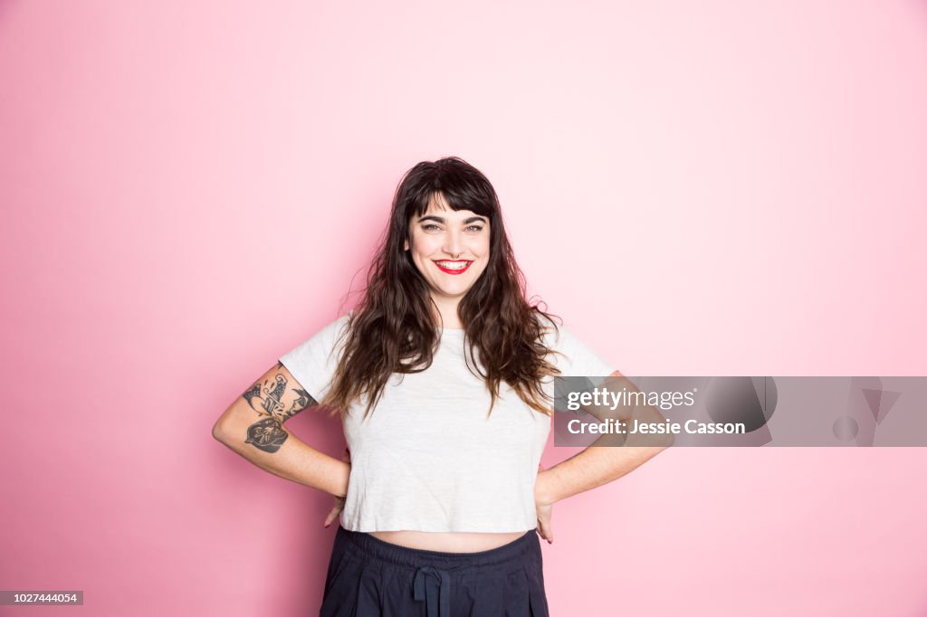 Portrait of a Woman with tattoos and red lipstick against a pink background