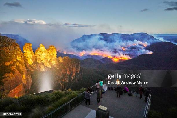 three sisters floodlit at dusk, queen elizabeth lookout, viewing platform with tourists watching and photographing fire, bushfire in jamison valley, blue mountains national park, australia - australia wildfires photos et images de collection