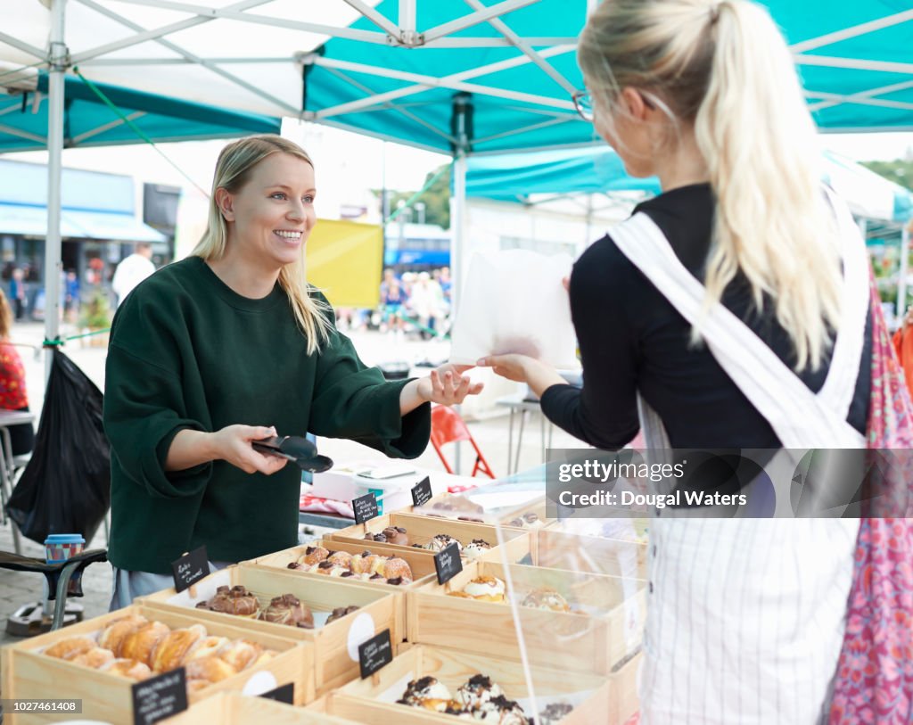 Woman selling homemade cakes on a local market and serving customer.