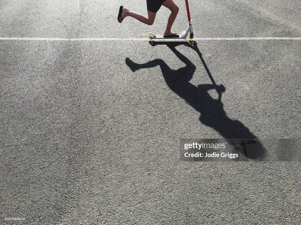 Shadow of a young girl riding a scooter along a painted line outside