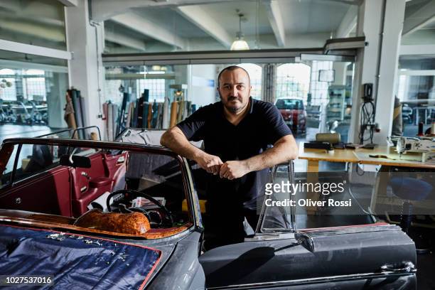 portrait of man at vintage car in an automobile upholstery workshop - oldtimerauto stockfoto's en -beelden
