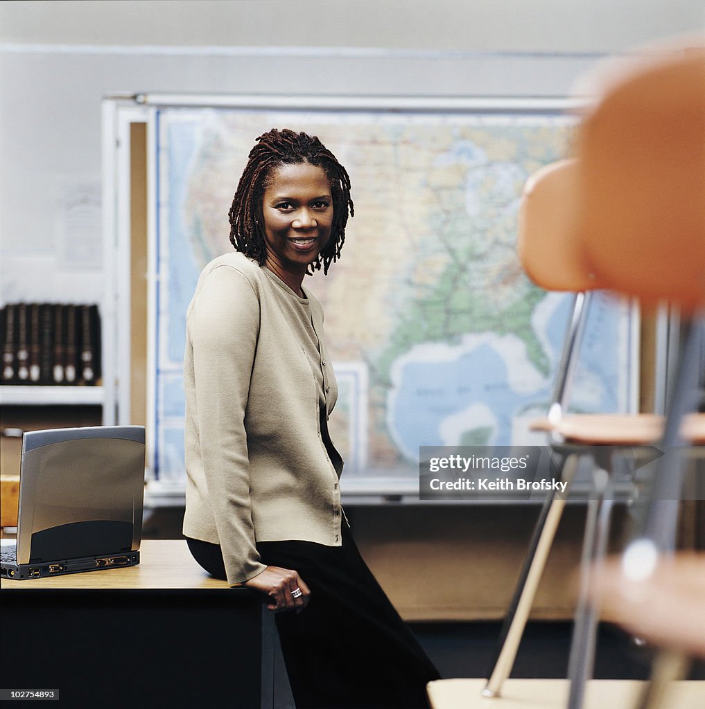 African American teacher sitting on desk in classroom