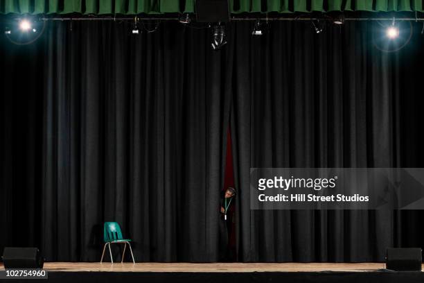 student peering from behind curtain on stage - theater stock-fotos und bilder