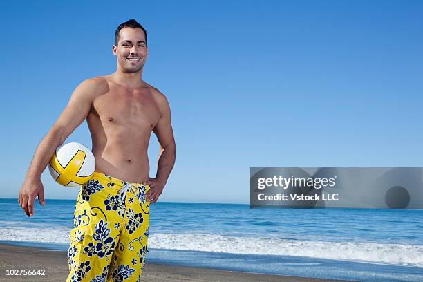 man with a beach ball standing on an oceanside beach - costume da bagno foto e immagini stock