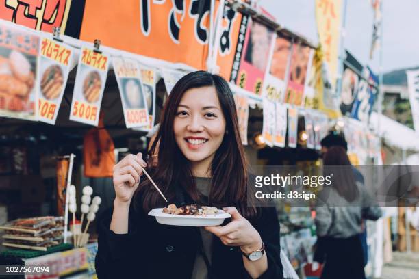 joyful female tourist enjoying japanese style snacks from local street vendor while travelling in japan - 日本食 個照片及圖片檔