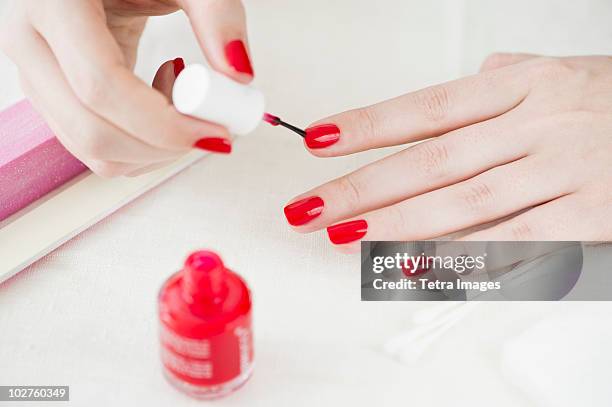 woman painting her nails with red nail polish - rode nagellak stockfoto's en -beelden