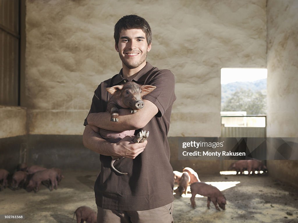 Man holding a piglet in pen