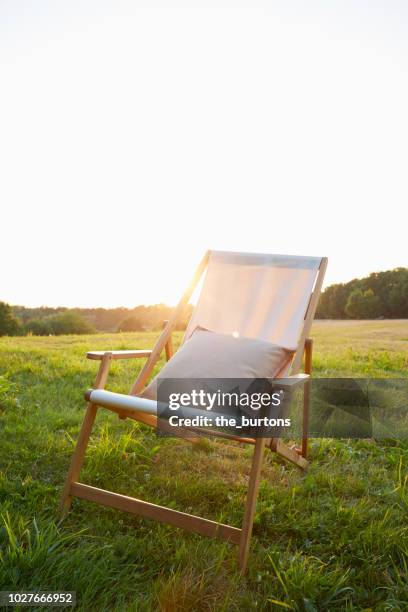 deck chair with pillow on meadow at sunset - folding chair stock-fotos und bilder