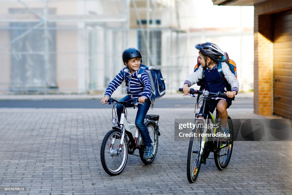 Two school kid boys in safety helmet riding with bike in the city with backpacks. Happy children in colorful clothes biking on bicycles on way to school. Safe way for kids outdoors to school