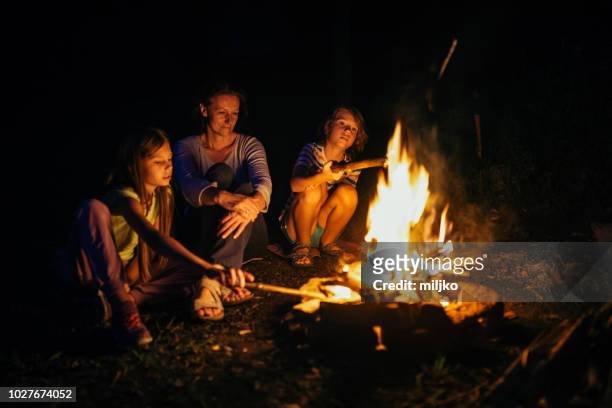 mother sitting next to the campfire with her children - fogueira de acampamento imagens e fotografias de stock