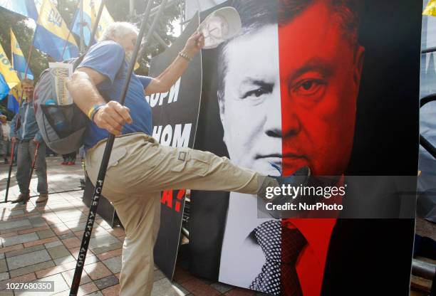 An Ukrainian protester beats a poster with an image of combo portrait depicturing faces of Ukrainian President Poroshenko and ex-President Viktor...