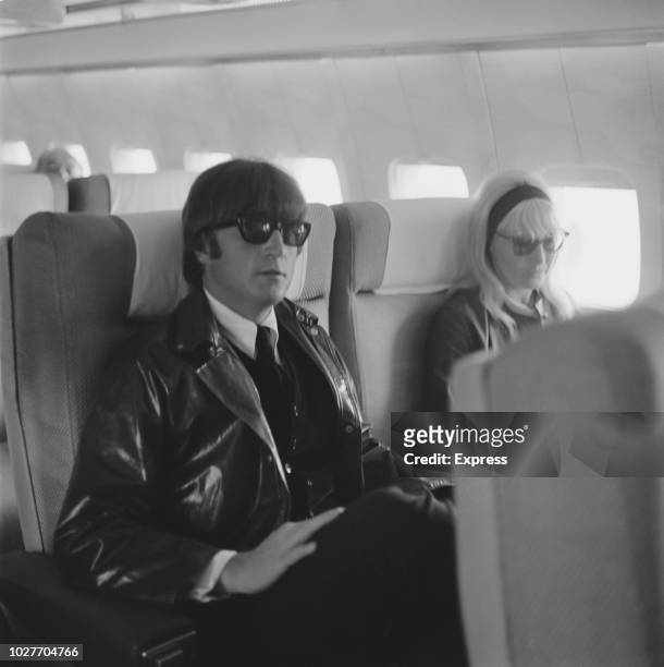 English singer, songwriter, and peace activist John Lennon of the Beatles with his wife Cynthia sitting on an airplane, UK, 28th May 1964.