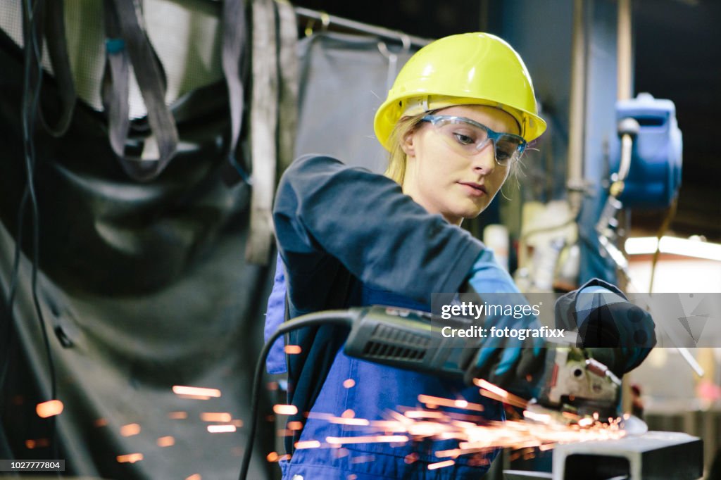 Junge weibliche Auszubildende Schweißnähte Stahl mit Mahlwerk in Werkstatt