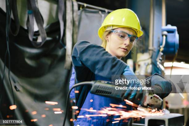 jonge vrouwelijke stagiair lassen staal met grinder in werkplaats - metaalwerker stockfoto's en -beelden