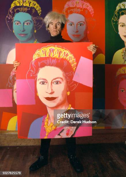 Portrait of American Pop artist Andy Warhol as he holds a silkscreen print of British monarch Queen Elizabeth II in his studio, the Factory, New...