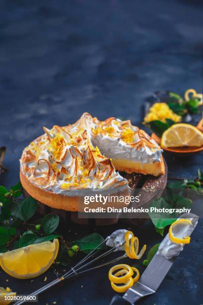 lemon tart with meringue, leaves, lemon zest, spatula and whisk on a dark background. a missing piece of the pie. home cooked desserts concept - merengue imagens e fotografias de stock