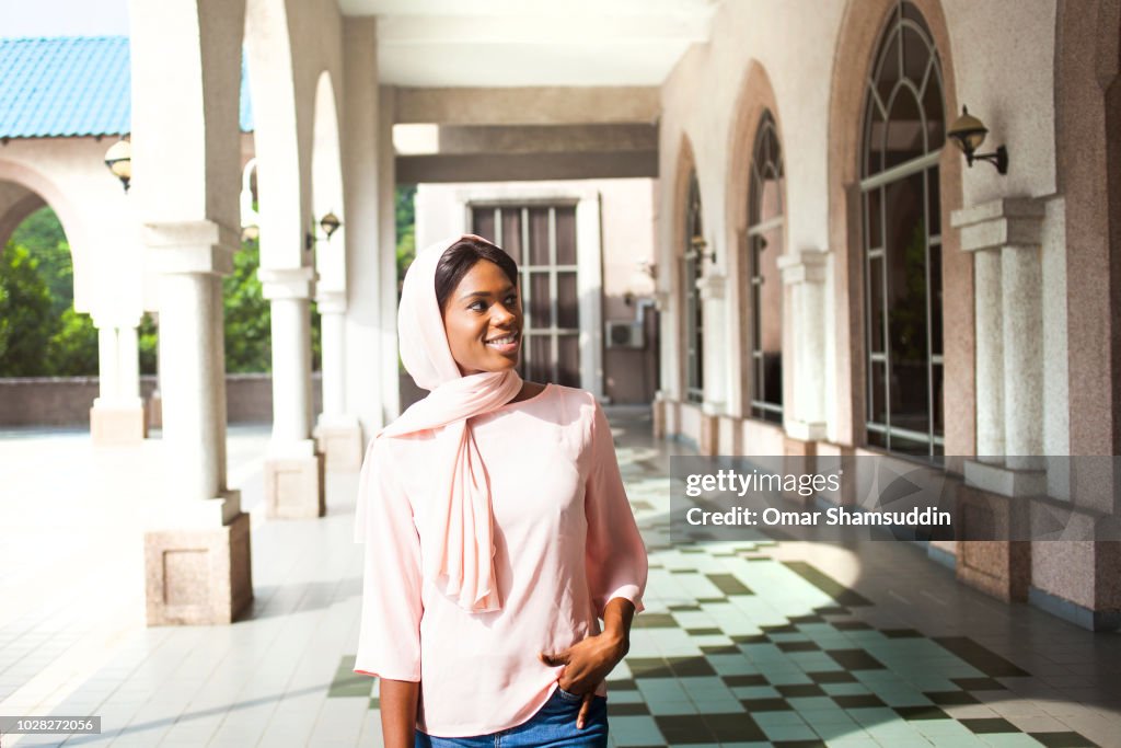 Black young girl in hijab smiling while walking in university campus