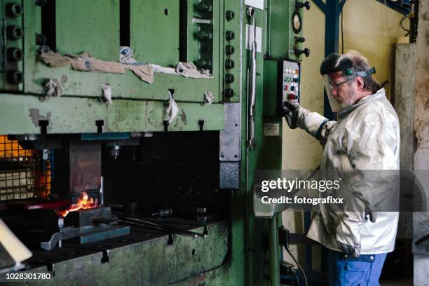 male blue collar worker works with hot iron at a hydraulic press - hydraulics stock pictures, royalty-free photos & images