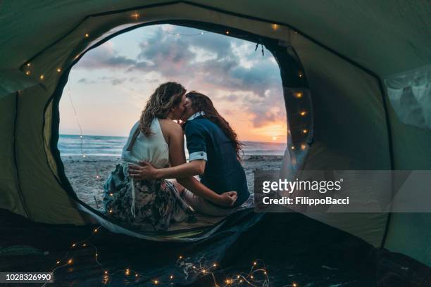 young adult couple admiring the sunset in a tent on the beach - lesbians kissing stock pictures, royalty-free photos & images