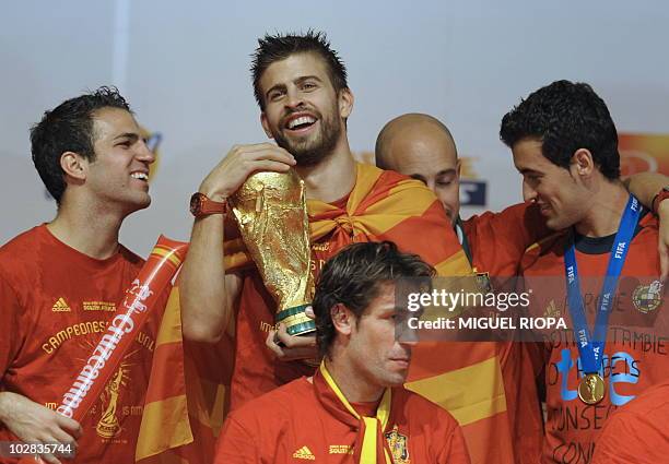 Spain's defender Gerard Pique hugs the trophy next to team mates on a stage set up for the Spanish team victory ceremony in Madrid on July 12, 2010 a...