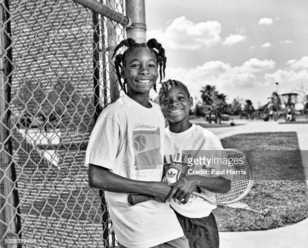 Portrait of American tennis players and sisters Venus Williams and Serena Williams as they pose beside the fence at the Compton tennis courts, South...