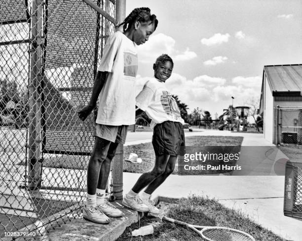 Portrait of American tennis players and sisters Venus Williams and Serena Williams as they hang onto the fence at the Compton tennis courts, South...