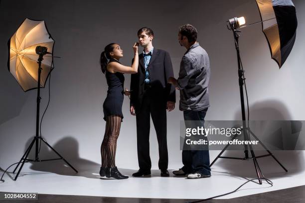 makeup artist and wardrobe stylist working on actor behind the scenes on a film set - cosmetics industry stock pictures, royalty-free photos & images
