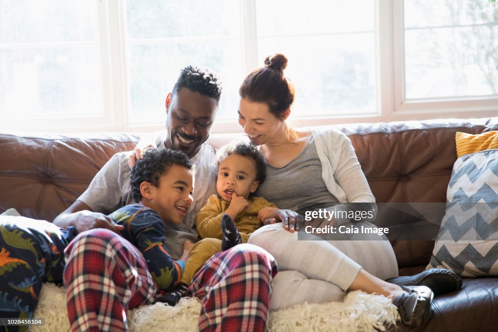 Multi-ethnic young family relaxing in pajamas on living room sofa